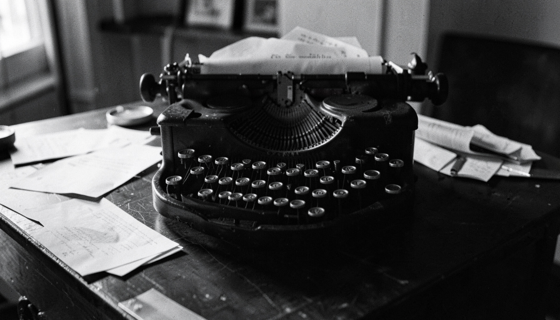 Vintage typewriter on a dark desk with scattered papers, moody black and white tones