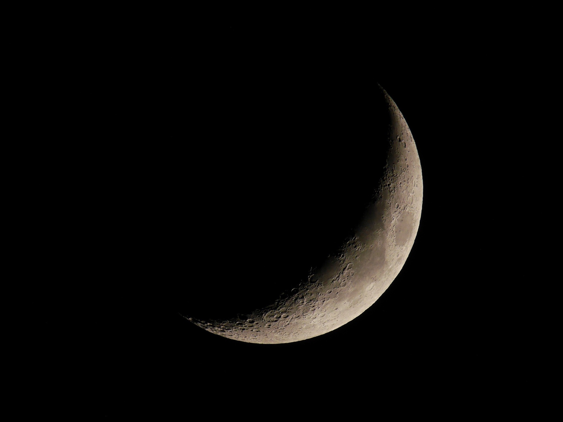 Close-up of a crescent moon with visible craters against a black night sky, grayscale tones, calm and serene mood