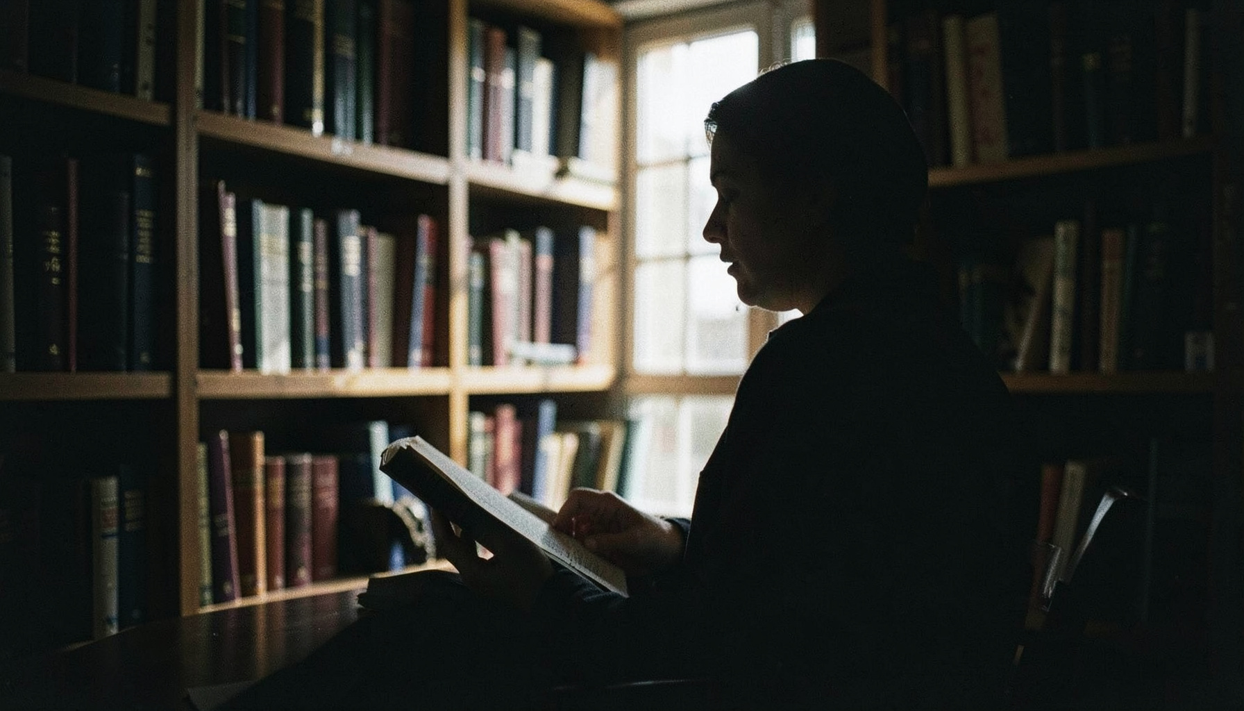 Portrait silhouette of a reader in a dim study surrounded by bookshelves, dark and atmospheric tones